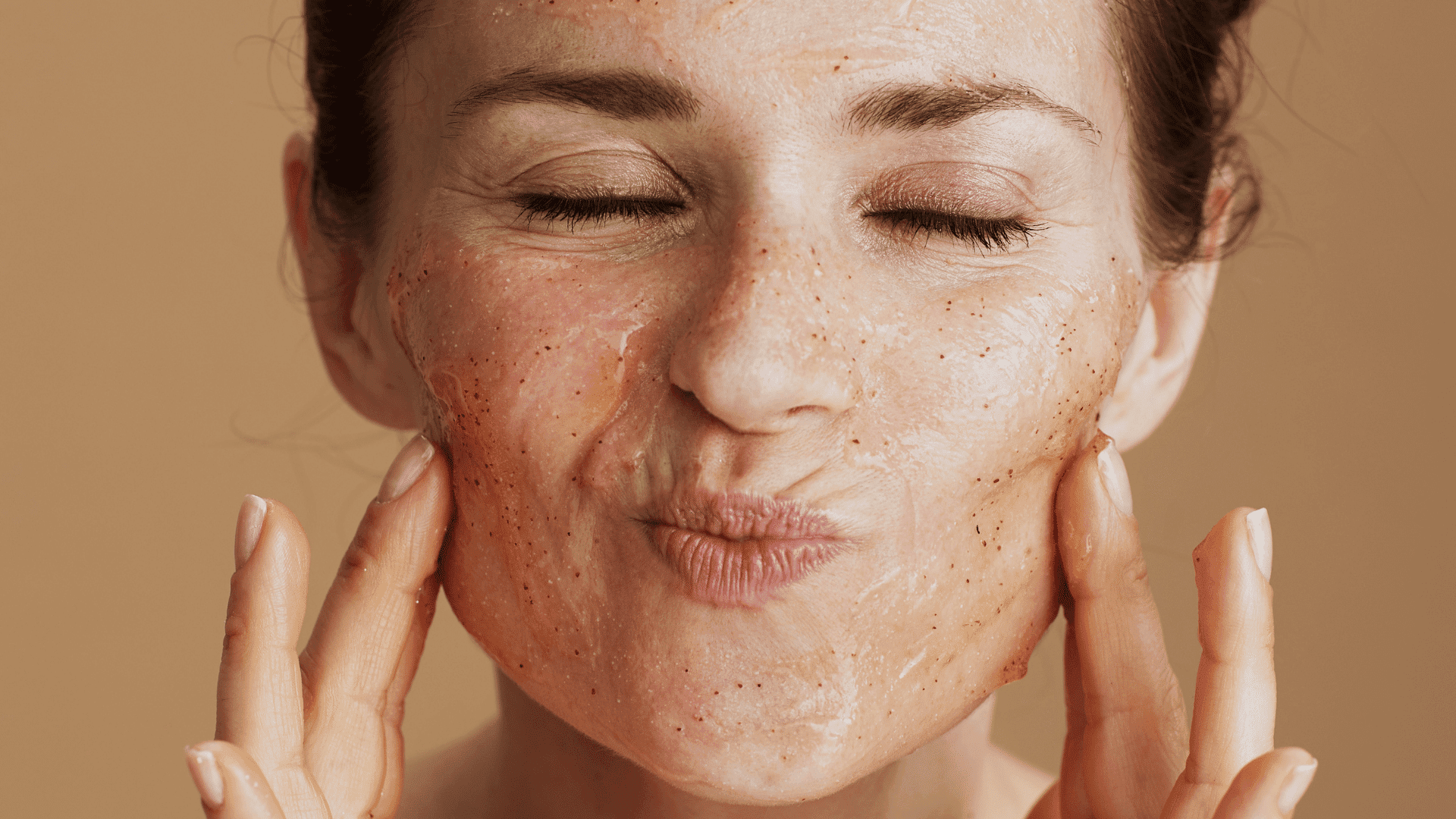 Facial scrub application, woman gently exfoliates skin with a textured cream.